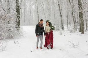 Schöne Braut und Bräutigam mit einem weißen Hund stehen auf dem Hintergrund eines verschneiten Waldes. foto