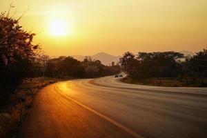 landstraße mit fahrenden autos und schönem goldenem sonnenunterganghintergrund in thailand.