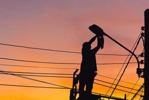 silhouette des elektrikers, der die beleuchtung an der led-straßenlaterne überprüft, techniker mit beschneidungspfad und wartungsdienstkonzepten foto