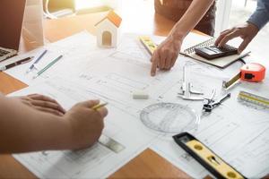 Hände des Architekten oder Ingenieurs mit Zeichenkompass mit Blaupause auf dem Schreibtisch im Büro. Team von Architekteningenieuren diskutiert und überprüft Dokumente und Geschäftsabläufe. Baukonzept. foto