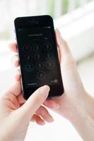 Hand der jungen Frau, die das Apple Iphone 5 hält und Passcode eingibt. das mobiltelefon wird von apple computer, inc. hergestellt foto