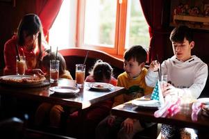 Kinder an Geburtstagen sitzen am Tisch und essen Pizza. foto