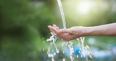 Wasser, das in die Hand der Frau auf Naturhintergrund gießt, Umweltprobleme foto