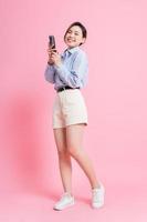Bild in voller Länge des jungen asiatischen Mädchens, das Smartphone auf rosa Hintergrund verwendet foto