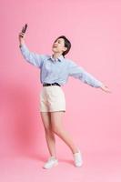 Bild in voller Länge des jungen asiatischen Mädchens, das Smartphone auf rosa Hintergrund verwendet foto