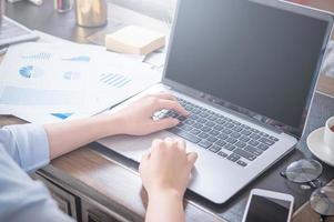 Unternehmenskonzept. Frau im blauen Hemd, die auf dem Computer mit Kaffee auf dem Bürotisch tippt, Hintergrundbeleuchtung, Sonnenblendeffekt, Nahaufnahme, Seitenansicht, Kopierraum foto