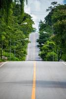 die schöne lange straße, die durch den wald in der landschaft von thailand führt. foto