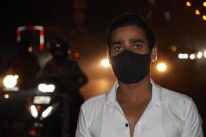 Ein junger Mann auf der Straße mit Maske, der Fotos bei schlechten Lichtverhältnissen im Freien trägt