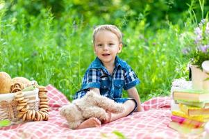 Ein kleiner süßer Junge sitzt auf einem Plaid und spielt mit seinem Teddybär.