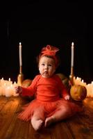 kleines Mädchen sitzt auf einem Hintergrund von Jack-Kürbissen und Kerzen auf schwarzem Hintergrund.