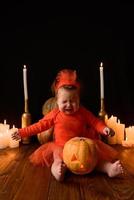 kleines Mädchen sitzt auf einem Hintergrund von Jack-Kürbissen und Kerzen auf schwarzem Hintergrund. foto
