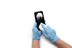 männliche hände in medizinischen handschuhen behandeln das telefon mit einem antiseptikum, um kein coronavirus zu bekommen. isoliert auf weißem Hintergrund. foto
