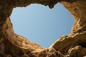 Steinhöhle mit einem herzförmigen Loch auf dem Dach. Blauer Himmel aus der Höhle gesehen. Algarve, Portugal foto