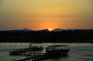 Sonnenuntergang am Meer mit Pier und Bergen foto