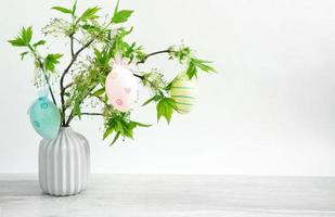 Ein Strauß grüner Zweige mit blühenden frischen Blättern in einer Vase auf dem Tisch ist mit bunten Ostereiern geschmückt. dekor im innenraum des hauses zu ostern. Platz kopieren foto