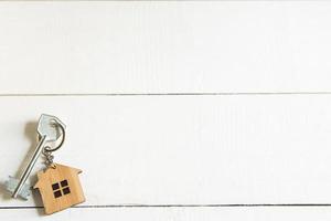 Schlüsselanhänger in Form eines Holzhauses mit Schlüssel auf weißem Hintergrund mit einem quadratischen Blatt für Notizen. Bau, Design, Projekt, Umzug in ein neues Haus, Hypothek, Miete und Kauf von Immobilien. Platz kopieren foto