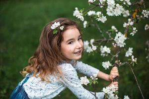 Ein süßes kleines Mädchen von 5 Jahren in einem blühenden weißen Apfelgarten im Frühling. Frühling, Obstgarten, Blüte, Allergie, Frühlingsduft, Zärtlichkeit, Fürsorge für die Natur. Porträt foto