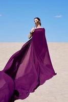 erstaunlich schöne brünette frau mit der pfauenfeder in lila stoff in der wüste. orientalisch, indisch, mode, stilkonzept foto