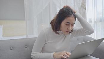 gestresste junge frau, die den kopf in den händen hält und auf den laptop-bildschirm schaut, probleme mit dem projekt hat und auf dem sofa im wohnzimmer sitzt. foto