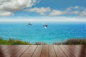 Oberseite des Holztisches mit Meer und zwei Delphinen im Hintergrund - leer, bereit für Ihre Produktdisplay-Montage. konzept des strandes im sommer foto