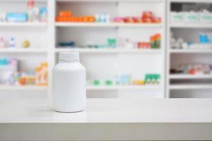 leere weiße Medizinflasche auf der Theke mit verschwommenen Medikamentenregalen in der Apotheke foto