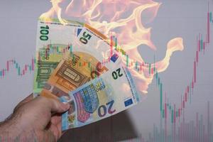 Hand, die drei brennende Euro-Banknoten mit einem Diagramm aus dem Finanzwesen hält foto