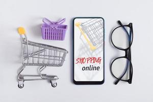 online-shopping flach legen kreative komposition. Knolling mit Telefon, Einkaufswagen und Gläsern foto