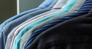 Schließen Sie eine Sammlung von Hemden in verschiedenen Farben, die sich im Schrank oder Kleiderständer aufreihen. klassisches Männeroutfit foto
