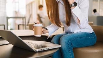Frau benutzt Laptop und tippt auf Laptop und hält Kaffeetasse im Café, Heimbüro foto