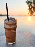 kaffee smooties kühles trinkwasser auf dem tisch holz meer und orange sonnenuntergang auf wasser hintergrund foto