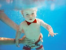 Kleiner Junge mit rotem Schmetterling, der im Schwimmbad unter Wasser taucht, schwimmen lernen. sport- und urlaubskonzept foto