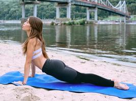 Junge fitte Frau in Sportbekleidung in verschiedenen Yoga-Asanas im Freien am Strand am Fluss. yoga- und sportkonzept foto