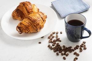 leckere, appetitliche, knusprige Croissants, heißer Kaffee in der blauen Tasse und Küchentuch auf Teller auf Marmortisch foto