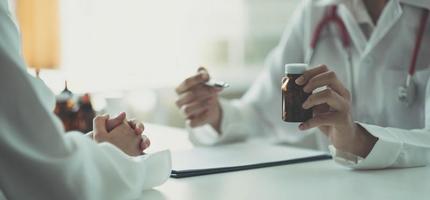 der Arzt und der Patient sprachen über etwas, während sie am Tisch saßen. ein arzt hält eine flasche mit medikamenten in der hand, die die art des medikaments ausführlich erklärt. foto