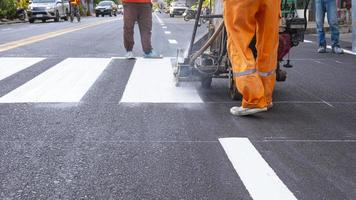 Der untere Teil der Straßenarbeitergruppe mit thermoplastischer Sprühmarkierungsmaschine malt Fußgängerüberwege auf Asphaltstraßen in der Stadt foto