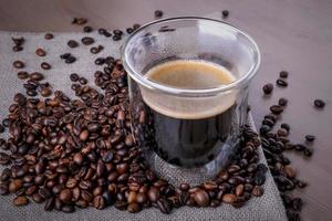 Glastasse mit Kaffee und Haufen gerösteter Kaffeebohnen foto