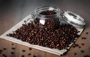 Glasgefäß mit gerösteten Kaffeebohnen auf Bohnenhaufen foto
