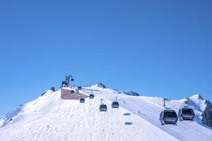 Seilbahnen, die sich über schneebedeckte Berge gegen den strahlend blauen Himmel bewegen foto