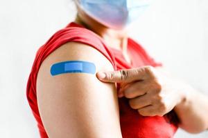 Am Arm der Frau ist ein blaues Pflaster befestigt. konzept für erste hilfe nach der impfung gegen coronavirus covid-19 und professionell, medizinisch, nadel, blut, krebs. Nahaufnahme, weißer unscharfer Hintergrund foto