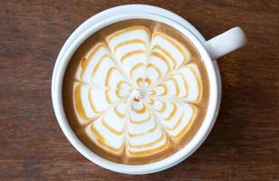 Nahaufnahme der Latte-Kaffeekunst mit Karamell auf der Wasseroberfläche, die auf dem Holztisch serviert wird. foto
