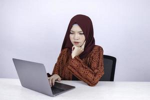 junge asiatische islamfrau ist ernster blick mit denkender geste hand auf gesicht auf der vorderseite des laptops. foto