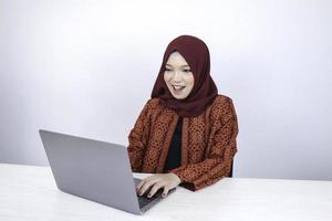 junge asiatische islamfrau mit kopftuch ist schockiert und aufgeregt über das, was sie auf dem laptop auf dem tisch sieht. foto