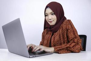 Junge asiatische Islamfrau sitzt und lächelt, wenn sie am Laptop auf weißem Hintergrund arbeitet. foto