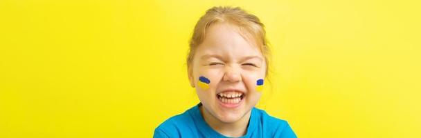 lächelndes Mädchen mit einer bemalten ukrainischen Flagge in Gelb und Blau auf ihren Wangen