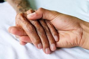 Hände des alten Mannes und eine Männerhand auf dem weißen Bett foto