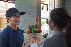 Lieferung eines asiatischen Mannes, der eine Tüte mit Lebensmitteln an eine Kundin an der Tür handhabt. foto