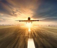 Flugzeug, das über die Start- und Landebahn des Flughafens fliegt, mit Stadtbild und Sonnenuntergang am Himmelshintergrund