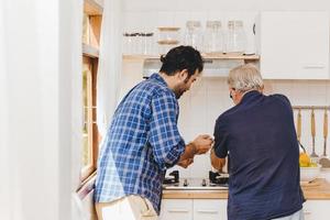 älterer kocht in der küche mit einem jungen mann der familie, um gemeinsam zu hause zu bleiben.