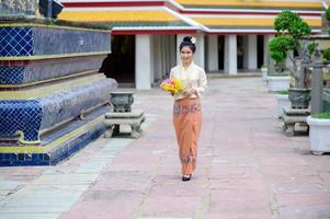 attraktive thailändische frau in einem alten thailändischen kleid hält frische blumen, die buddha huldigen, um sich auf dem traditionellen songkran-fest in thailand etwas zu wünschen foto