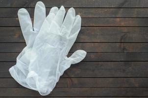 weiße einweghandschuhe auf dunklem holzhintergrund. handschuhe zum schutz vor coronavirus. foto